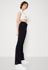 Høyt liv, mørkeblå corduroy bukser med flair og synlige sømmer samt en teksturert overflate. Båret med en cropped hvit topp og hvite sneakers.