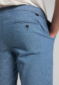 Pantalones cortos de mezclilla en un azul claro con un acabado texturizado, que cuentan con un bolsillo trasero con un cierre de botón negro y una cinturilla elástica suave.