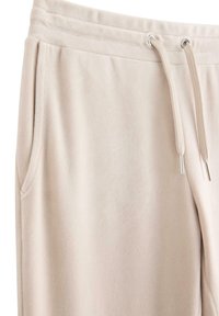 Pantalon de survêtement en tissu doux beige avec poches latérales et taille à cordon de serrage avec œillets et embouts en métal.