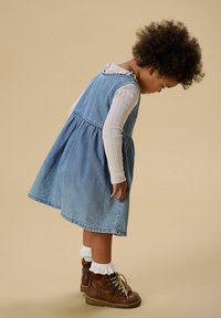 Džinsu kleita ar izpletušos svārku un volānveida izgriezumu, kombinēta ar teksturētu garroku topu un brūnām mežģīnēm audzējamām zābaciņām ar baltām zeķēm.