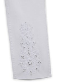 Pantaloni in denim bianco con intricate ricami floreali bianchi lungo il lato, dettagli a taglio e una texture liscia.
