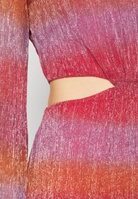 Tessuto a maglia con sfumature di rosa e viola, caratterizzato da una lucentezza metallica, maniche lunghe e un dettaglio a cut-out in vita.