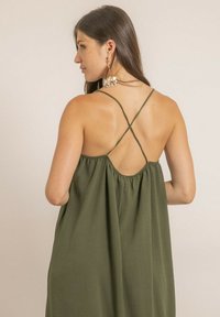 Robe sans manches vert olive avec des détails de bretelles croisées dans le dos, présentant une coupe ample et un tissu doux et texturé.