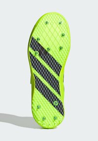 Semelle néon verte brillante avec surface texturée, présentant un motif en croix et des rayures noires diagonales. Comprend plusieurs pointes pour une meilleure adhérence.