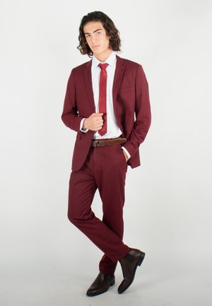 Costume bordeaux avec cravate assortie, chemise blanche et ceinture marron. Coupe slim avec chaussures habillées marron brillantes. Texture lisse, design ajusté.
