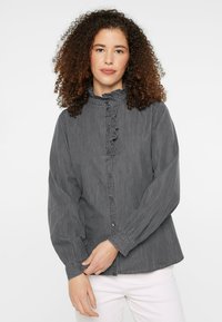 Gray button-up shirt features a ruffled collar, long sleeves, and a relaxed fit with a soft fabric texture. Accented with buttons down the front.