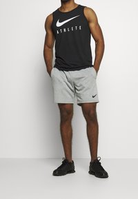 Czarny top sportowy Nike z napisem "ATHLETE", w połączeniu z szarymi szortami z małym logo Nike oraz czarnymi butami sportowymi.