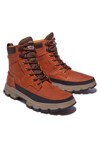Braun farbene Leder-Mid-Cut-Stiefel mit strukturiertem Finish, kontrastierender schwarzer Gummisohle, Metallösen und orangefarbenen Schnürsenkeln. Timberland-Logo sichtbar.