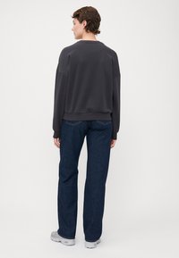 Gray sweatshirt with a relaxed fit, ribbed cuffs, and crew neckline, paired with dark blue straight-leg jeans and gray sneakers.
