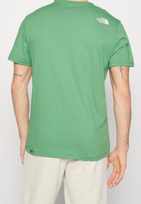 Green cotton t-shirt with a round neckline, short sleeves, and a logo on the upper back. Features a regular fit and smooth texture.