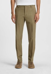 Pantalons khaki avec une texture lisse, design à jambes droites et devant plat. Portés avec des baskets en daim marron. Style minimaliste.