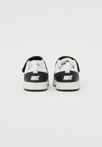 Baskets Nike noir et blanc avec une finition en cuir lisse, dotées d'une sangle en Velcro, d'une semelle en caoutchouc et d'un logo bien visible sur le talon.