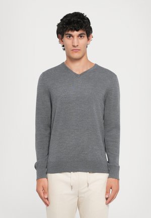 Grauer V-Ausschnitt-Pullover aus weichem Strickstoff, mit langen Ärmeln und lockerer Passform, kombiniert mit hellen Hosen.