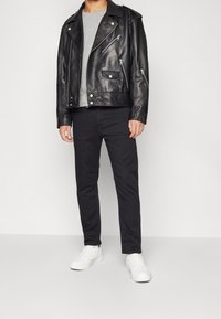 Chaqueta de cuero negra de motorista con cremalleras plateadas, camiseta de cuello redondo gris, pantalones negros ajustados y zapatillas blancas. Textura suave, corte moderno.