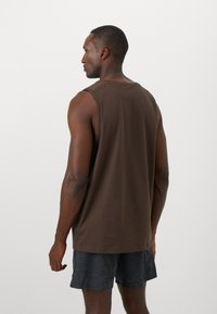 Brun bomuldsærmeless skjorte, afslappet pasform. Glat tekstur, minimalistisk design, rund halsudskæring, parret med mørke shorts.