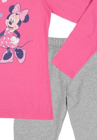 Top rosa a maniche lunghe con Minnie Mouse in un vestito rosa a pois, abbinato a pantaloni grigio chiaro, entrambi in tessuto morbido.