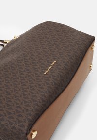 Ruskea kuvioitu keinonahkainen käsilaukku, jossa on kultaiset yksityiskohdat, tasainen pohja ja sileä vaaleanruskea nahkareunus.