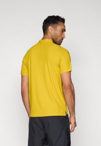 Κίτρινο κοντομάνικο πουκάμισο με υφή κυματοειδούς μοτίβου, με γιακά όρθιο και πλαϊνές σχισμές, σε συνδυασμό με σκούρες βερμούδες.