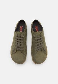 Scarpe verdi in suede con una superficie liscia, dotate di sei lacci grigi, punta rotonda e suola in gomma marrone. La scritta "CAMP" è stampata in rosso sulla soletta.