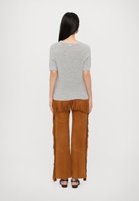 Haut gris côtelé à manches courtes associé à un pantalon en daim marron avec des détails à franges et des poches plaquées, complété par des sandales noires.