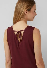 Bordeaux mouwloze top met een V-vormige rug en striksluiting. Gemaakt van gladde stof, met een schone, eenvoudige uitstraling zonder patronen.