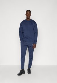 Sudadera y pantalones deportivos azul marino hechos de un tejido suave, con acentos del logo. El conjunto tiene un corte relajado y se combina con zapatillas deportivas negras.