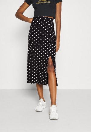 Falda midi negra con lunares y una abertura lateral, hecha de tela suave. Combinada con una camiseta negra corta y zapatillas blancas.