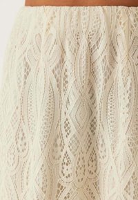 Spetskjol i off-white, med intrikata diamant- och virvlande mönster samt en texturerad yta och elastisk midja.