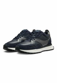 Marinblå sneakers med en kombination av mocka och läder, texturerade detaljer, platta skosnören och en kontrasterande vit mellansula.