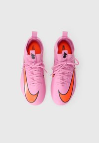 Roze synthetische voetbalschoenen met een gestructureerde afwerking, voorzien van zwarte en oranje Nike swoosh accenten en vetersluiting.