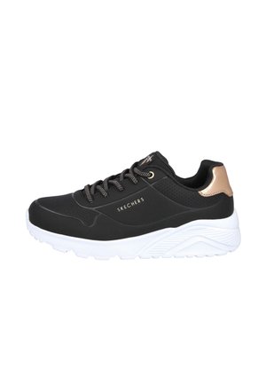 Zapatilla deportiva negra con parte superior de tela lisa, acentos dorados y suela de goma blanca con un patrón texturizado y diseño de cordones.