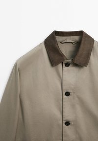 Kaki jas met een donkerbruine suède kraag, voorzien van zwarte knopen en een glad, gestructureerd stof. Ontwerp met knopen aan de voorkant en een nette afwerking.