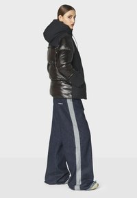 Giacca in nylon nera, imbottita e con cappuccio, caratterizzata da pannelli lucidi. Abbinata a pantaloni in denim a gamba larga con dettagli a strisce grigie.