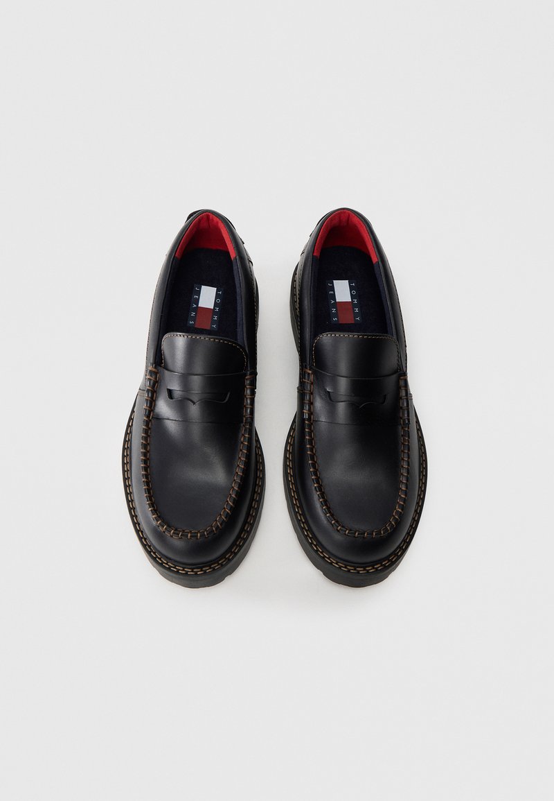 Mocassins en cuir noir avec couture visible, dessus texturé, doublure rouge et détail de logo sur les semelles intérieures. Design classique avec un bout rond.