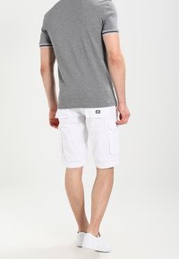 Polo shirt gris à manches courtes avec des poignets rayés, associé à un short cargo blanc avec des poches latérales et une coupe décontractée.