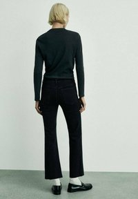 Svarta utsvängda jeans i kombination med en mörk långärmad tröja och svarta loafers. Vita strumpor synliga, textil med struktur och enkel design.