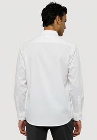 Bílá košile s dlouhými rukávy s klasickým límcem, knoflíkovými manžetami a hladkým, texturovaným materiálem s přiléhavým střihom.