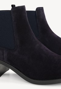 Bottes Chelsea en daim bleu marine foncé avec des panneaux latéraux élastiques et des talons bas empilés sur fond blanc.