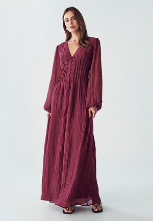 Maxi dress in deep purple, featuring textured fabric with vertical pleats, a V-neckline, button detailing down the front, and long sleeves.