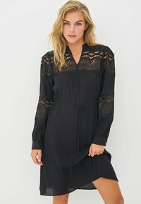 Must mustriga, millel on pikad varrukad, peene pitsi detailidega õlgadel ja varrukatel, V-kaelus ning vöö, et reguleerida sobivust.