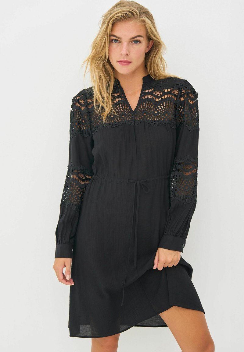 Must mustriga, millel on pikad varrukad, peene pitsi detailidega õlgadel ja varrukatel, V-kaelus ning vöö, et reguleerida sobivust.