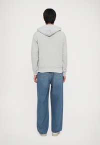 Sudadera gris con capucha hecha de una tela suave, combinada con jeans de mezclilla azul de pierna ancha con una cintura alta y dos bolsillos traseros.