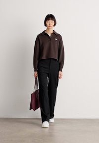 Brown cropped polo with a collar and logo, paired with black wide-leg trousers and white sneakers. Holding a burgundy tote bag.