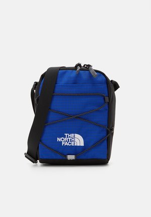 Sacoche en tissu bleu avec des accents noirs, dotée d'une poche zippée sur le devant, d'un design en cordon élastique et du logo The North Face.