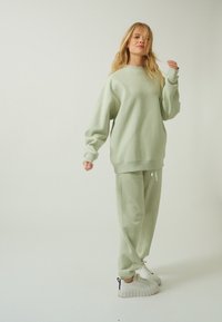 Lysegrøn sweatshirt og matchende joggingbukser lavet af blødt stof med en afslappet pasform. Sættet er kombineret med hvide sneakers.