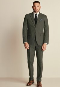 Dark green suit with a fitted blazer and slim trousers, white shirt, black tie, and brown shoes. Features subtle pinstripes and a pocket square.