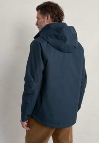 Chaqueta impermeable azul marino con capucha, que presenta una textura suave y un corte recto. La vista trasera muestra las costuras de los hombros y los detalles de las mangas.