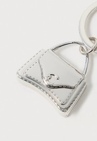 Breloc din metal argintiu în formă de poșetă mică, cu detalii cusute și un cârlig curbat pe un fundal alb.