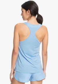 Ljusblå sporttop med racerback-design, tillverkad av stretchigt material, bärs tillsammans med matchande shorts. Har en mjuk textur.