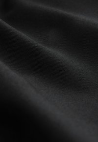 Fekete szövet sima, enyhén texturált felülettel; a redők lágy árnyékokat alkotnak, kiemelve gazdag, sötét színárnyalatát.